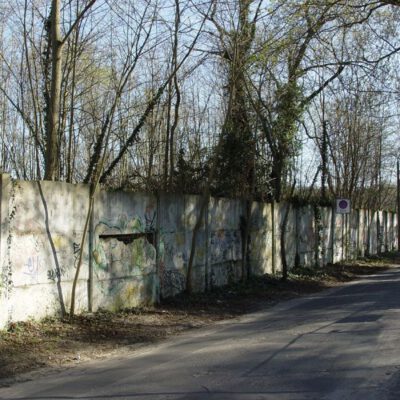 Farbaufnahme einer Baumumsäumten Straße mit Mauer: Die Hinterlandmauer an der Bertinistraße wurde erst 2011 abgetragen. Die Betonsegmente lagern im städtischen Bauhof der Landeshauptstadt Potsdam (2007) - Foto: Hans-Hermann Hertle