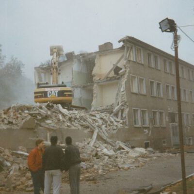 Ein zur Hälfte niedergerissenes Gebäude, im Bildvordergrund 3 Personen vor einem Schutthaufen: Bildreihe über den Abriss der Grenztruppen-Kaserne im Jahr 1992 - Foto: Privatbesitz