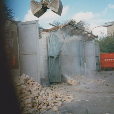 Ein Kranarm, dessen Greifer auf ein Werkstattgebäude greift, im Bildvordergrund Mauerziegelhaufen: Bildreihe über den Abriss der Grenztruppen-Kaserne im Jahr 1992 - Foto: Privatbesitz